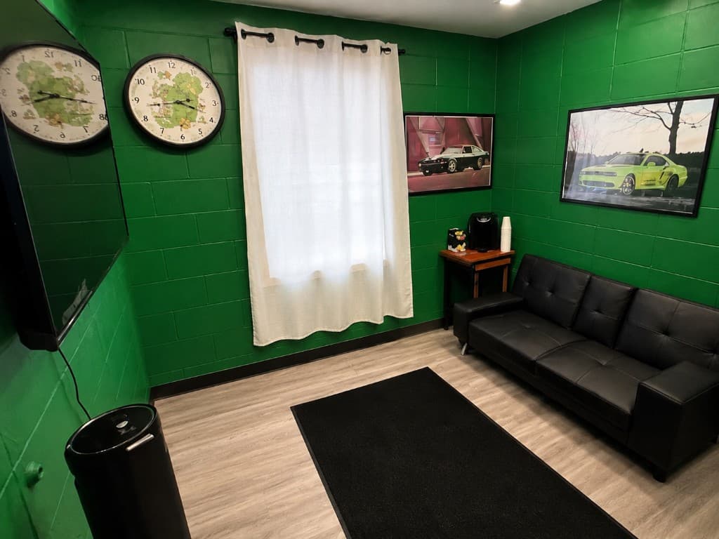 Doctor Detail waiting room — green cinder block walls, black sofa, TV, coffee maker, car posters, and window with curtain in Eagan MN